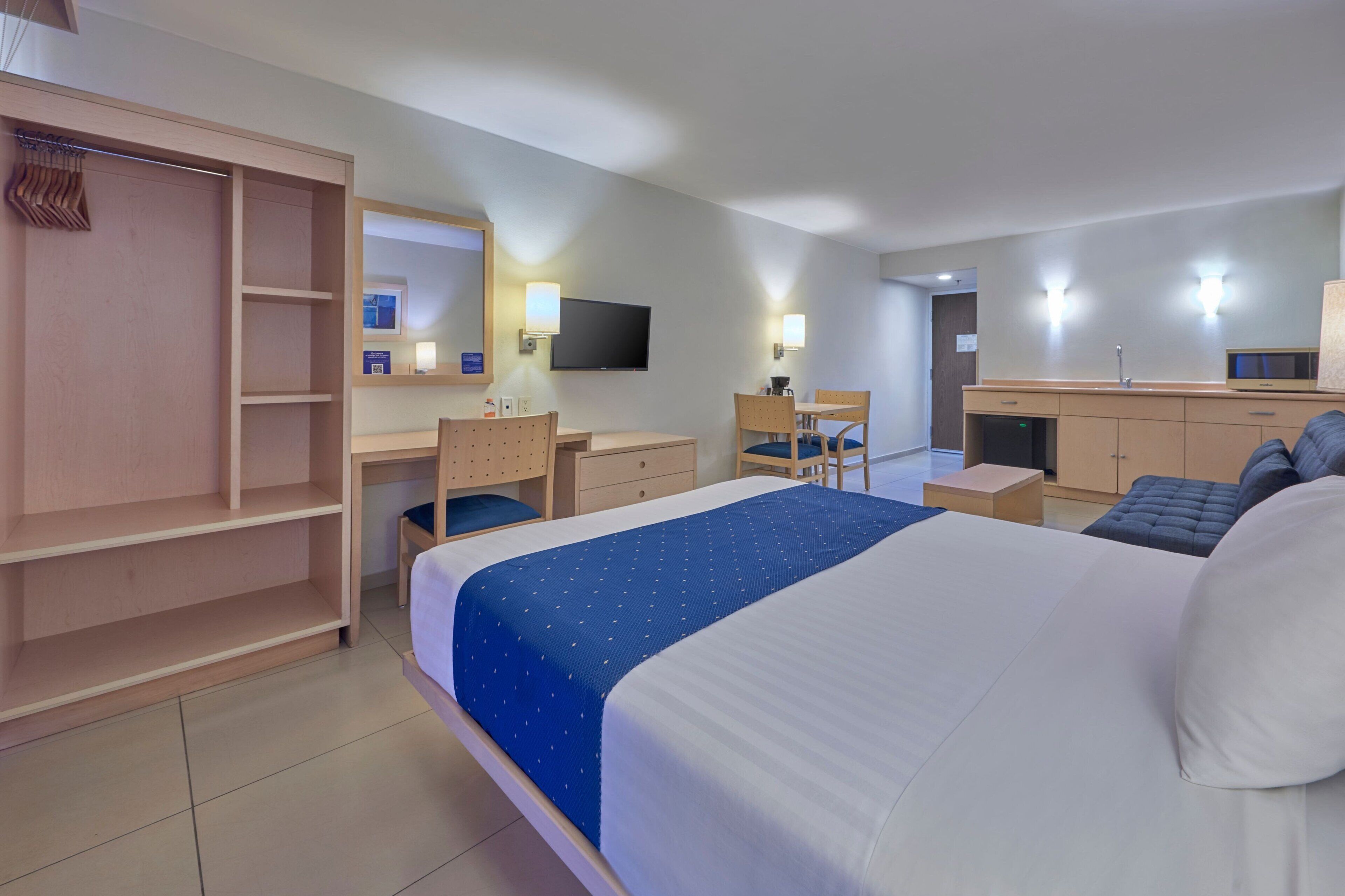 Una habitación de hotel con cama, escritorio, silla, armario y televisor.