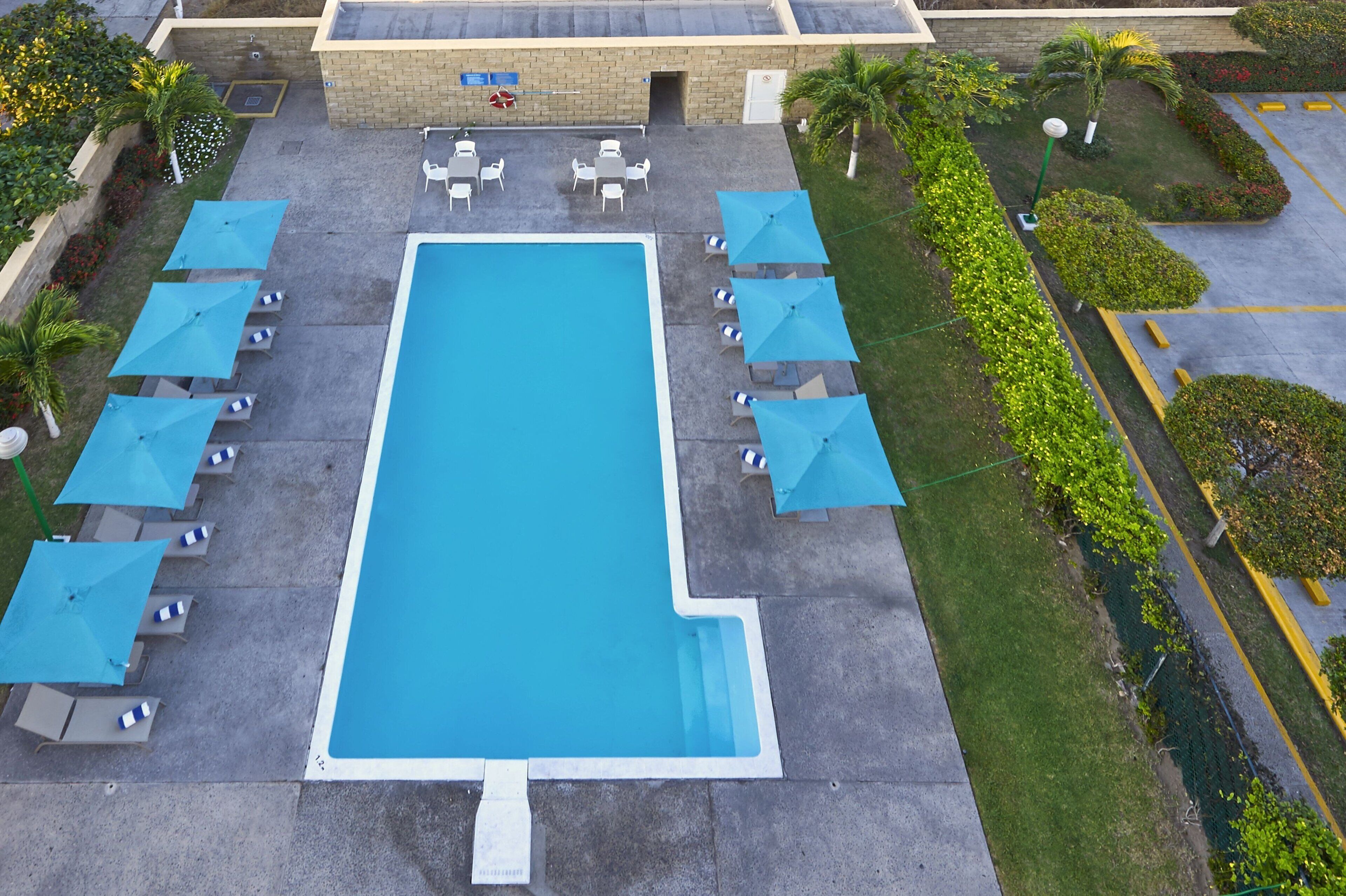 Una piscina rectangular con sombrillas azules y sillones de descanso a ambos lados.