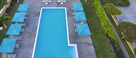 Una piscina rectangular con sombrillas azules y sillones de descanso a ambos lados.