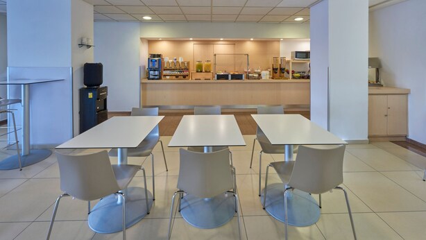 Una cafetería moderna con mesas y sillas blancas, una estación de café y un microondas.