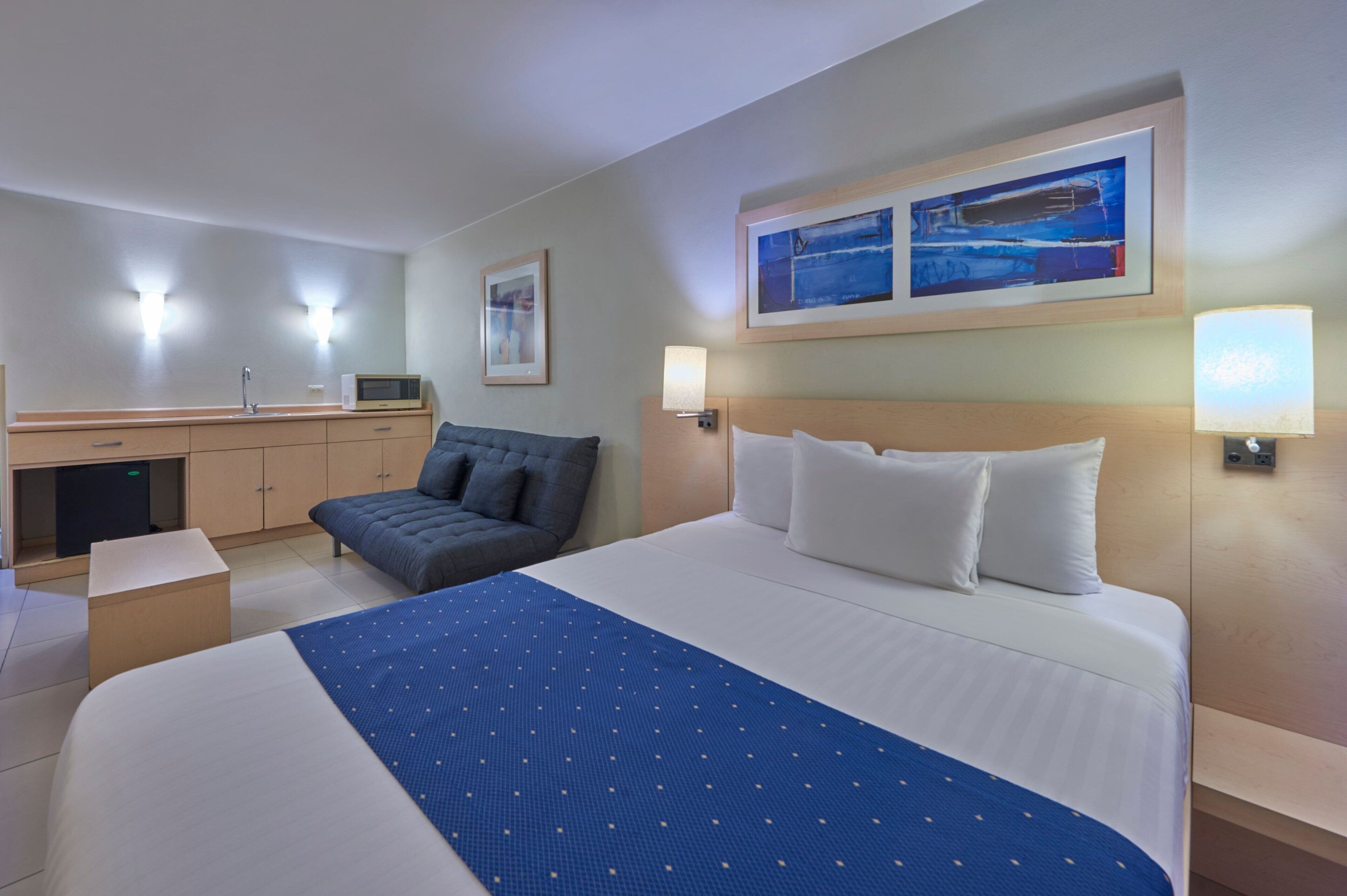 Ein Hotelzimmer mit einem großen Bett, einer Couch, einem Schreibtisch mit Computer und zwei Wandlampen.