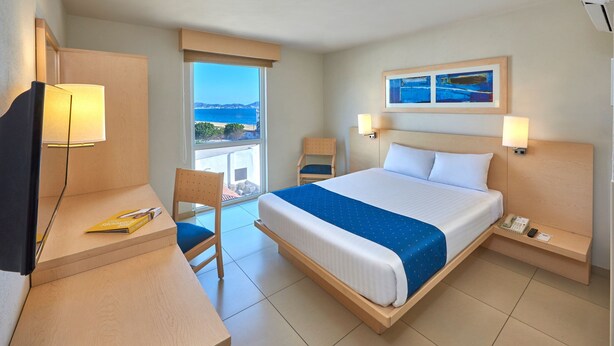 Ein Hotelzimmer mit Bett, Schreibtisch, Stuhl und Meerblick.