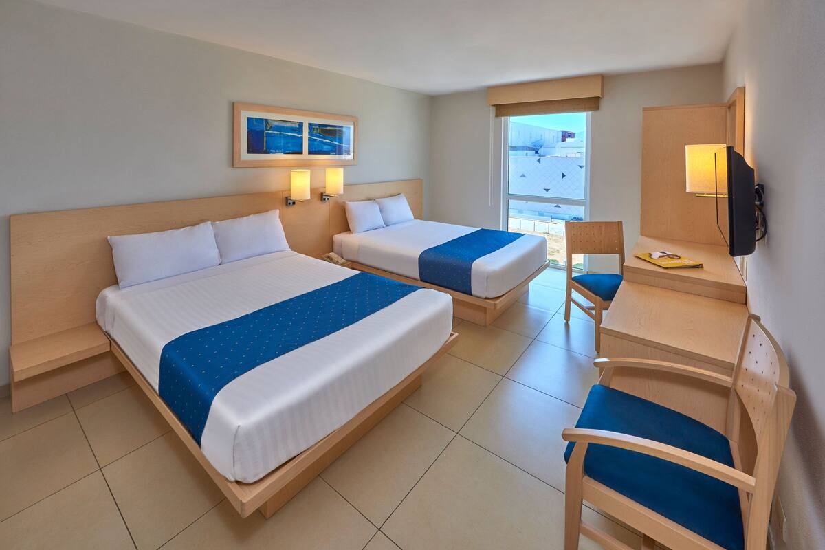 A hotel room with two beds, a desk, a chair, a TV, and a window with a view.