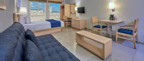 A hotel room with a bed, a sofa, a desk, a chair, a TV, and a window with a view.