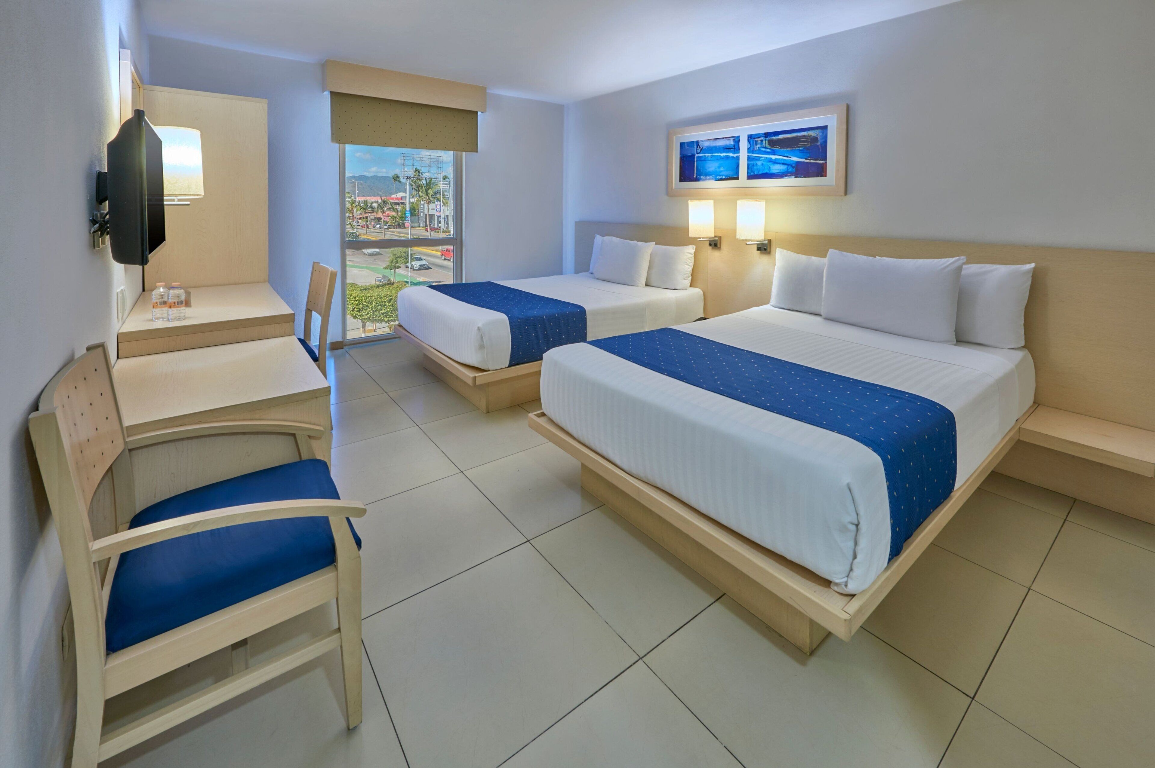 A hotel room with two beds, a desk, a chair, and a TV.