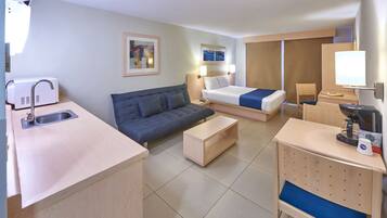 Ein Hotelzimmer mit einer Küchenzeile, einem Sofa, einem Bett, einem Schreibtisch und einem Stuhl.