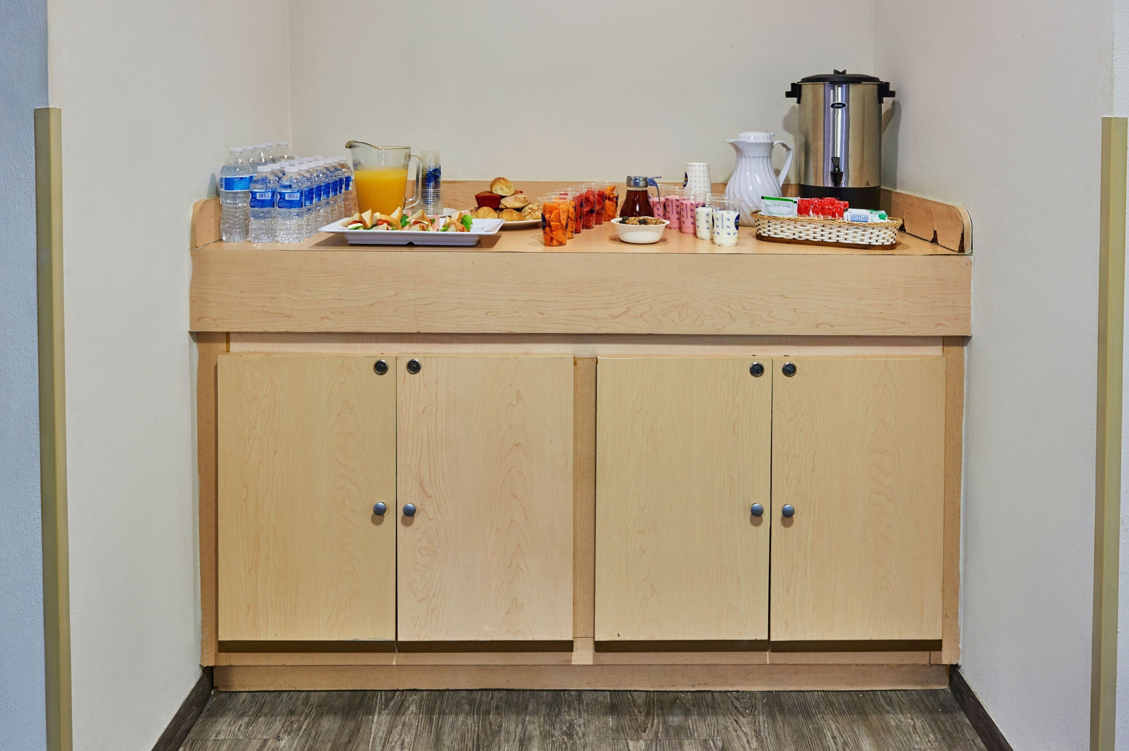A kitchenette with a wooden countertop, two cabinets, and various food items and beverages.