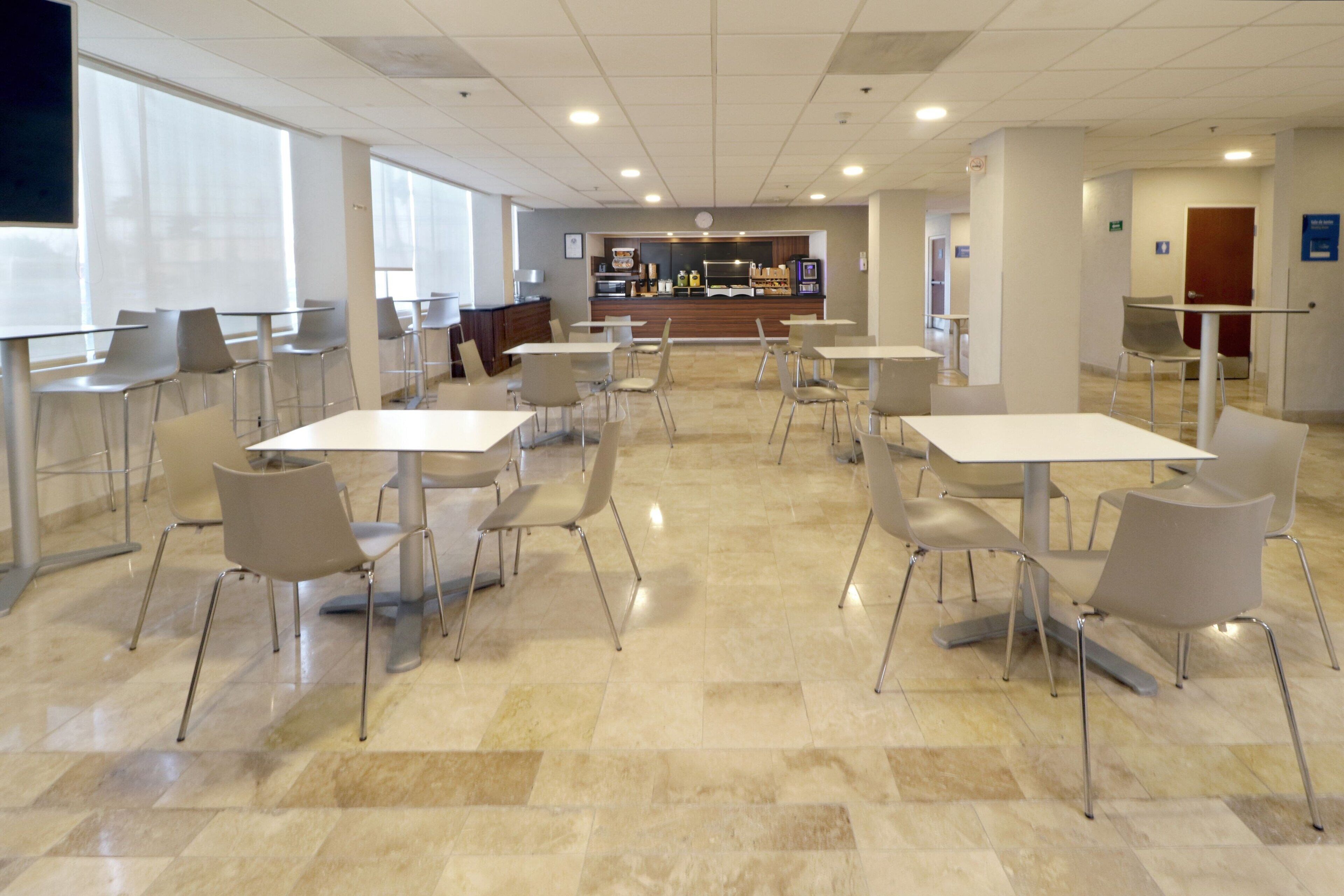 A spacious indoor area with multiple tables and chairs, a counter with a display, and a large window providing natural light.
