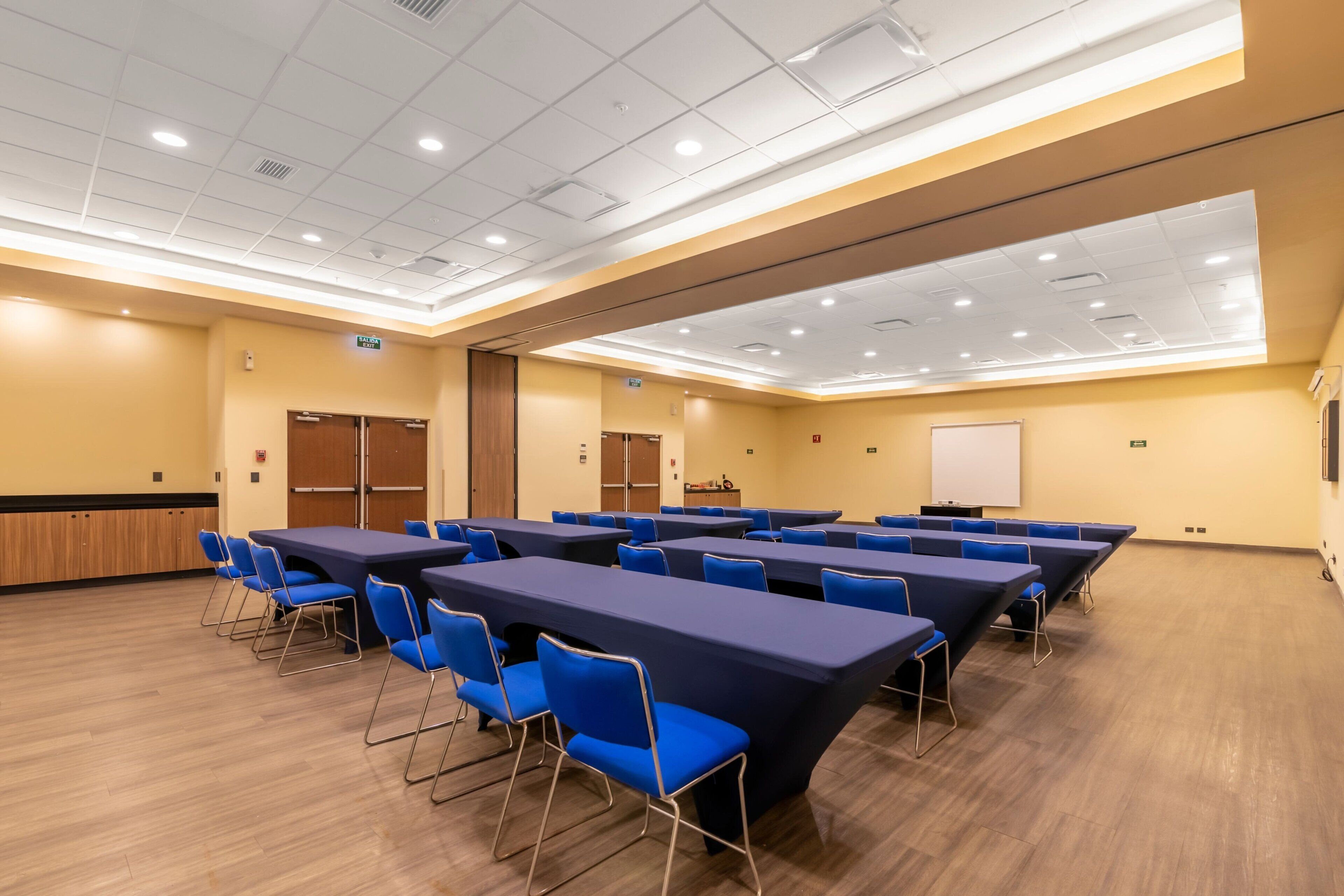 A conference room with multiple tables and chairs, a whiteboard, and a wooden panel wall.