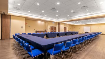 Uma sala de conferência com uma mesa comprida e cadeiras azuis, equipada com um quadro branco e um púlpito.