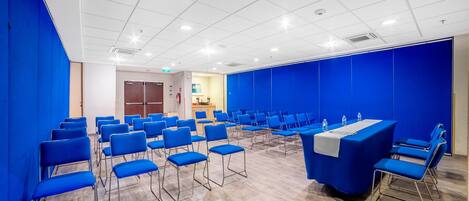 A conference room with rows of blue chairs, a long table with a white tablecloth, and a blue partition wall.