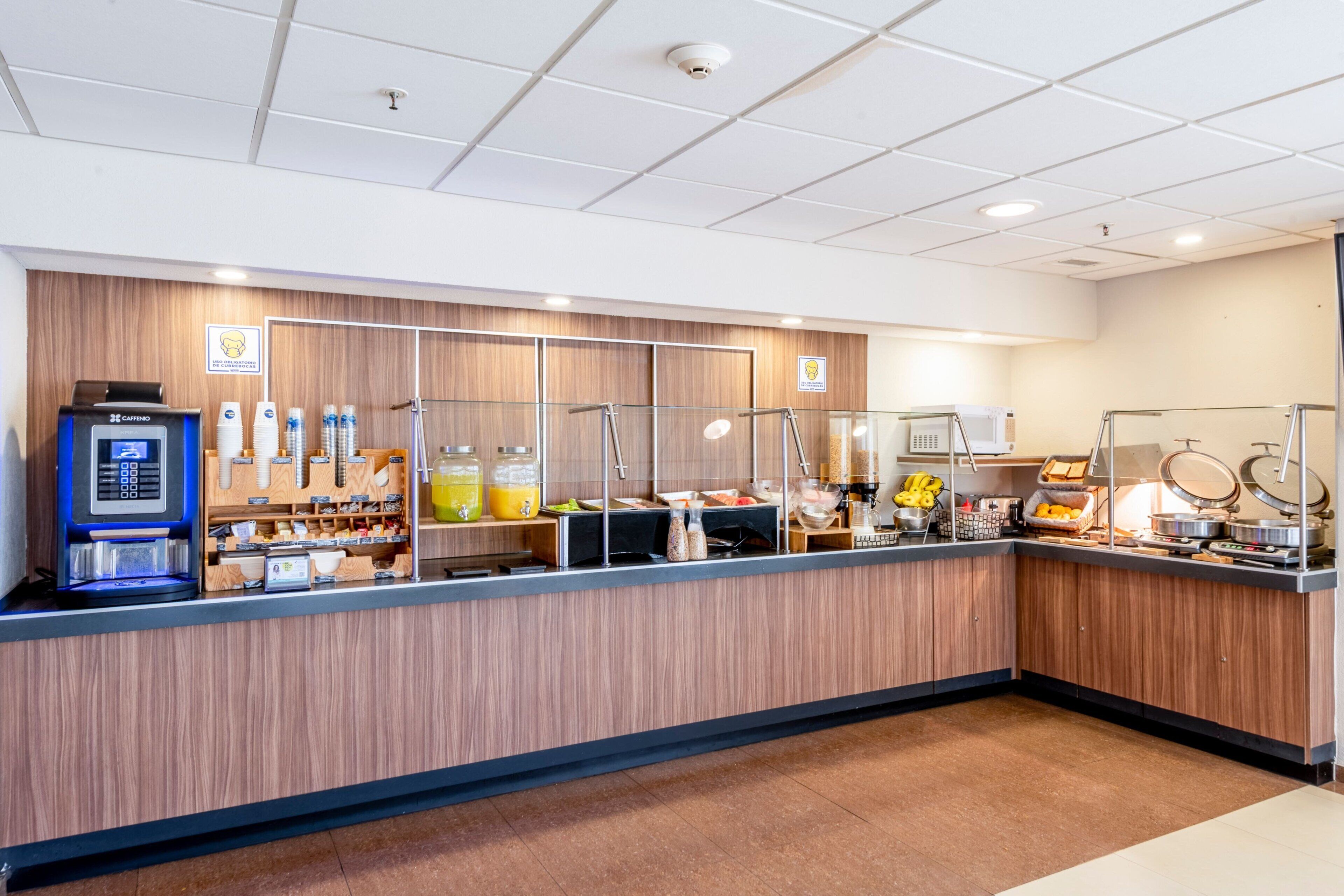 A self-service breakfast station with a coffee machine, fruit, and various food items.