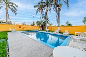A swimming pool with white lounge chairs and a yellow wall.