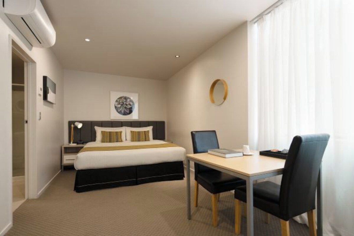 A hotel room with a bed, bedside table, lamp, and a desk with a chair.