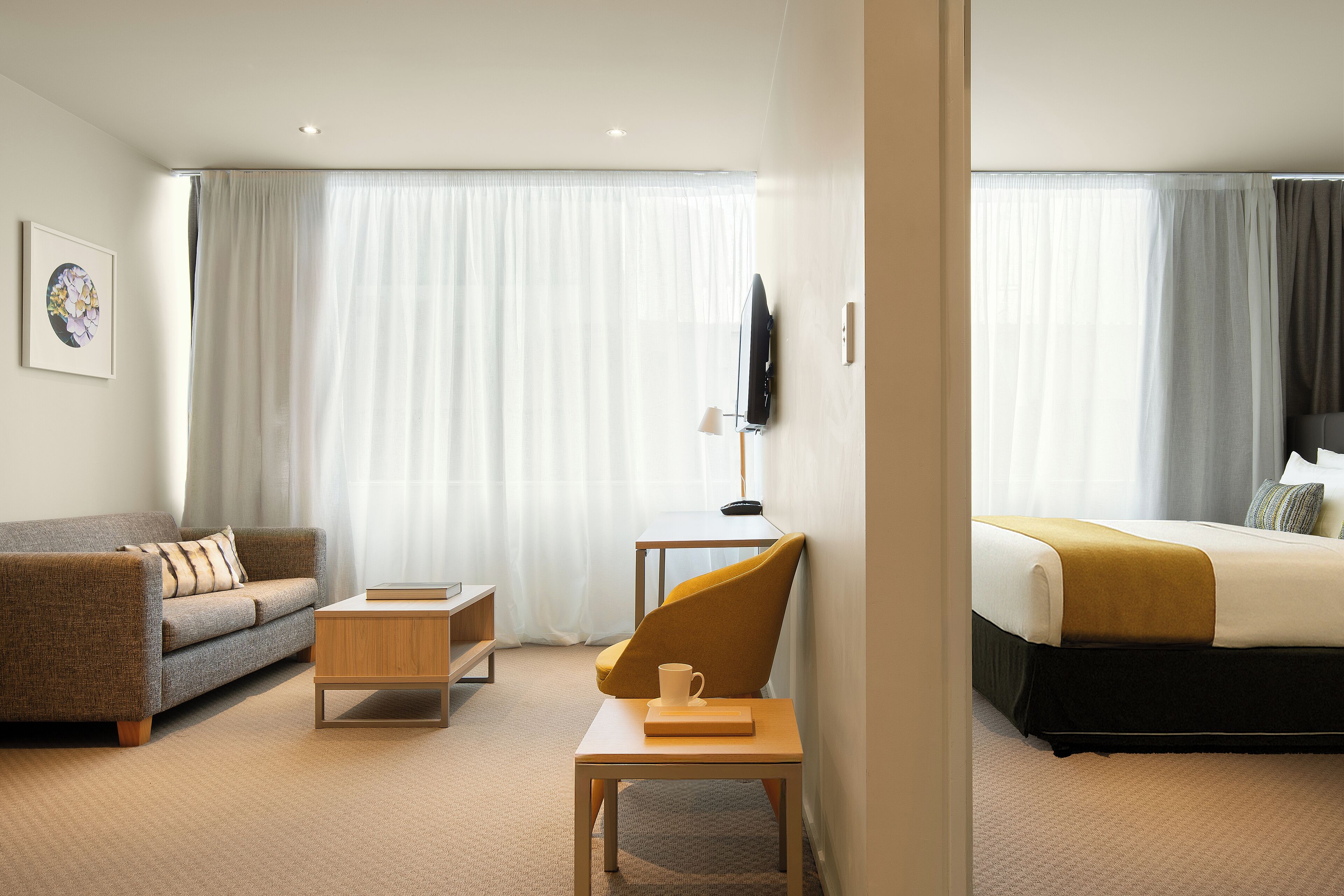 A hotel room with a sofa, a coffee table, a TV, and a bed with a headboard.