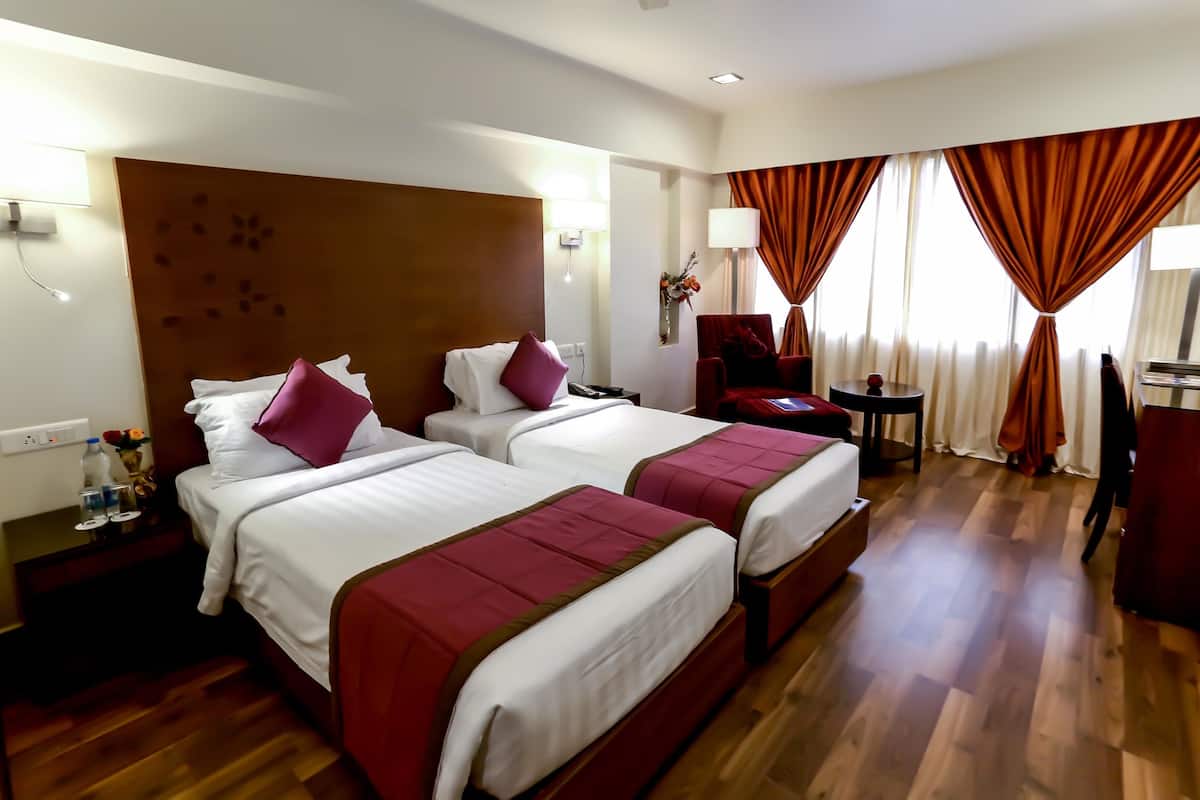 Ein Hotelzimmer mit zwei Betten, Holzboden, einem Schreibtisch, einem Stuhl und einem Vorhangfenster.