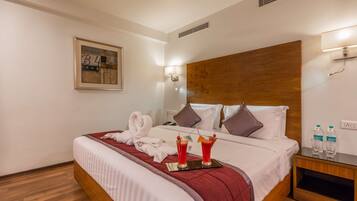 A hotel room with a wooden headboard, a neatly made bed with a red blanket, two bottles of water, and a framed picture on the wall.