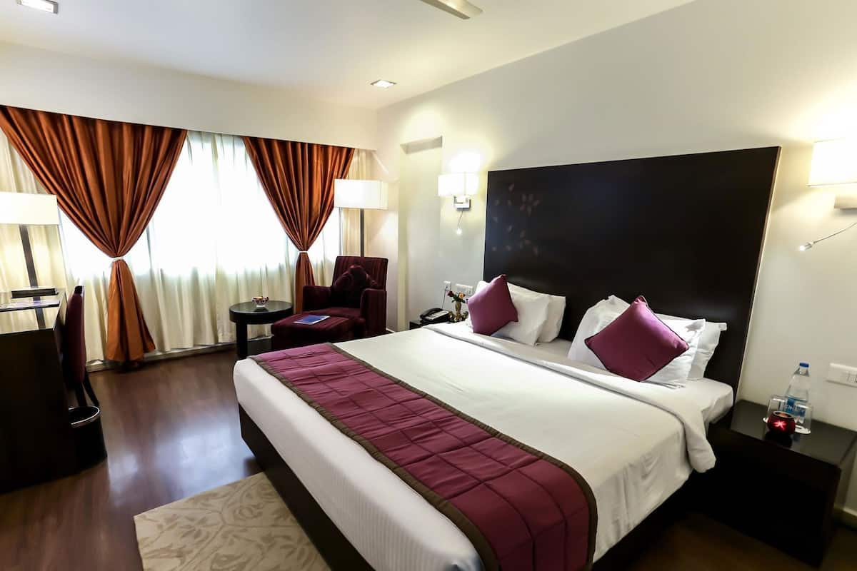 Ein Hotelzimmer mit einem großen Bett, einem Schreibtisch, einem Stuhl, einer Lampe und einem Nachttisch.