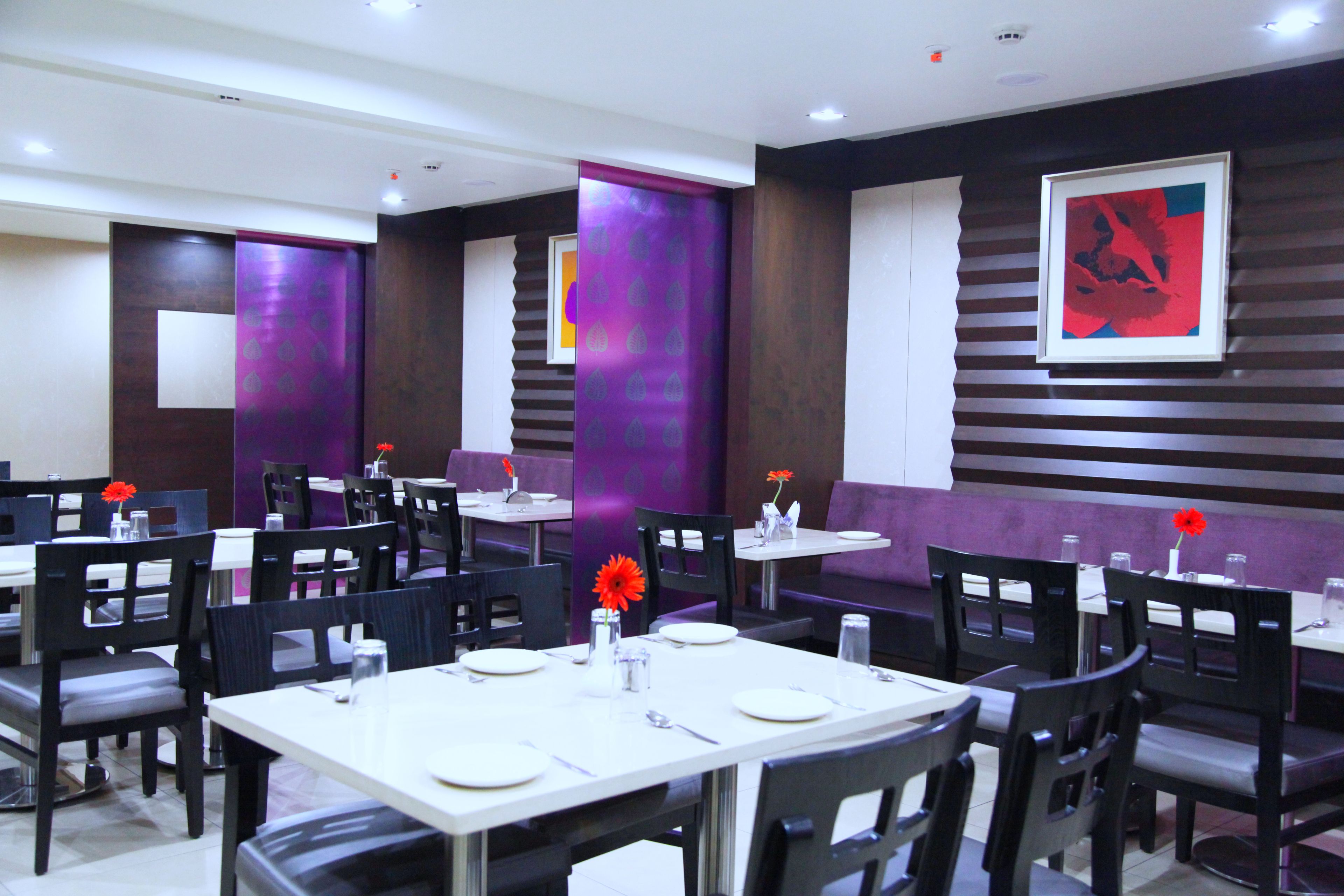 A restaurant with multiple tables and chairs, purple decorative panels, and a framed artwork on the wall.