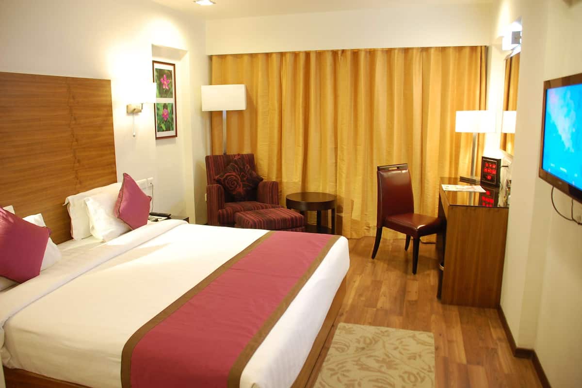 Ein Hotelzimmer mit einem großen Bett, einem Schreibtisch, einem Stuhl, einem Fernseher und einem Fenster mit Vorhängen.