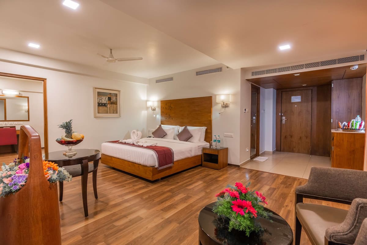 Ein Hotelzimmer mit einem hölzernen Bett, einem kleinen runden Tisch mit Blumenvase, einem Sessel und einem Holzschrank.