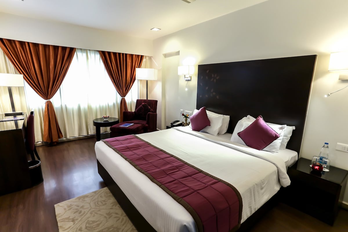 Ein Hotelzimmer mit einem großen Bett, einem Schreibtisch, einem Stuhl, einem Nachttisch und einer Lampe.