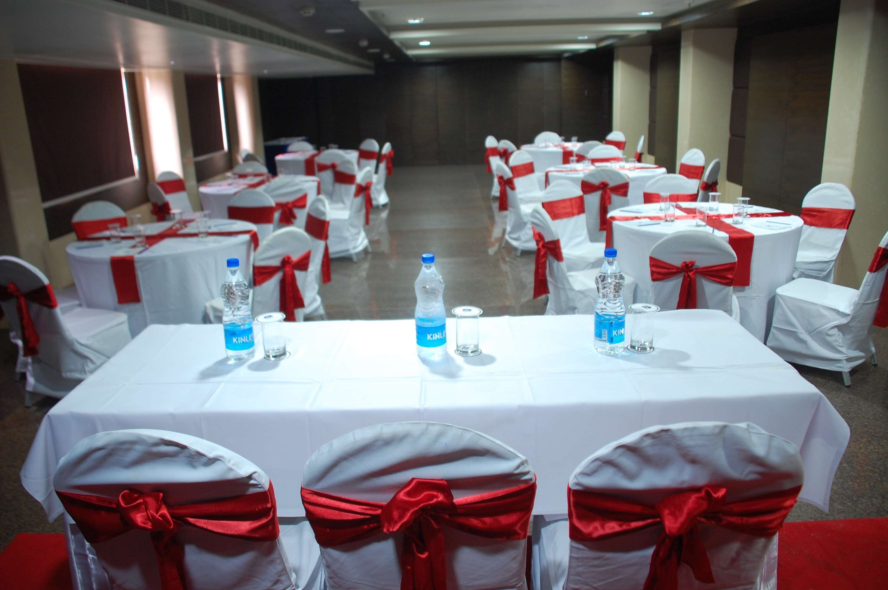A banquet hall with round tables and chairs, each with white tablecloths and red sashes.
