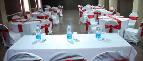 A banquet hall with round tables and chairs, each with white tablecloths and red sashes.