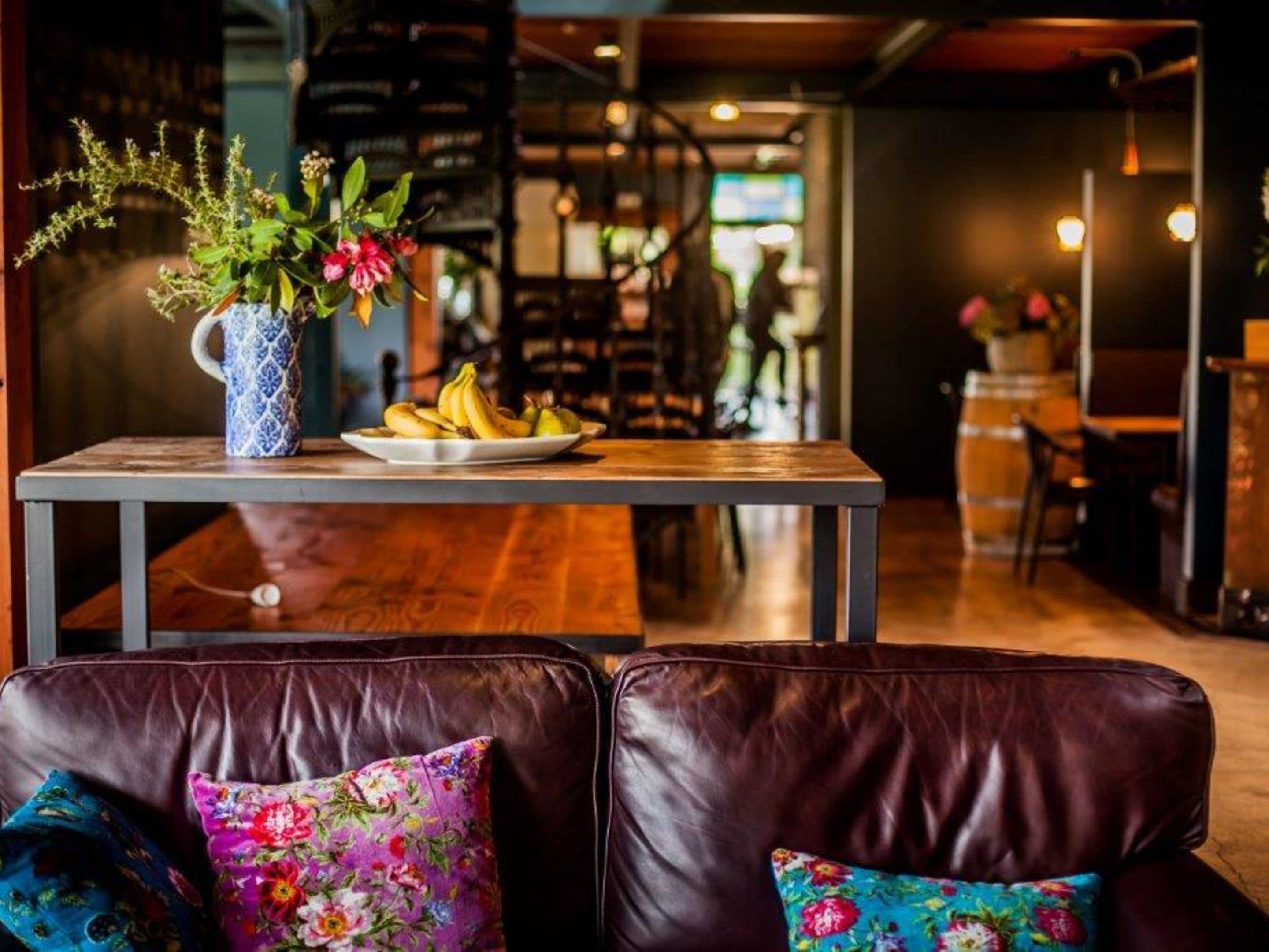 Un coin salon confortable avec une table en bois, un vase rempli de fleurs et une assiette de bananes.
