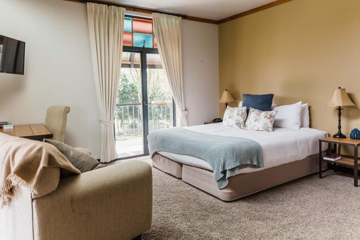 A hotel room with a bed, a chair, a desk, a TV, and a balcony with curtains.