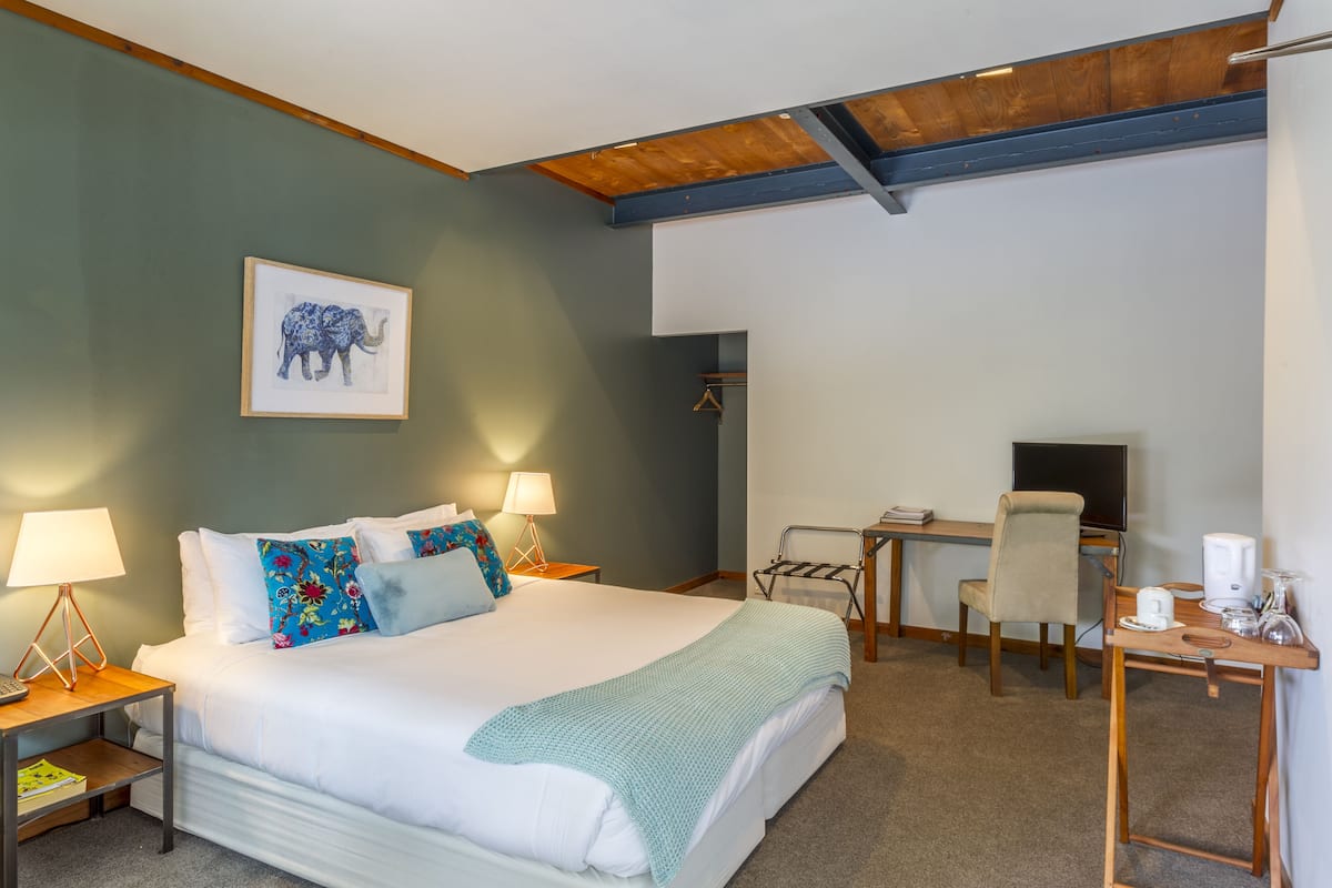 A hotel room with a bed, bedside tables, a desk, a chair, a television, and a framed picture on the wall.