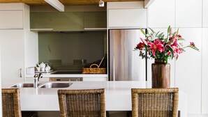 Una cocina moderna con una isla central, electrodomésticos de acero inoxidable, sillas de mimbre y un florero con flores.