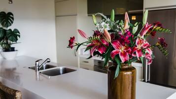 A modern kitchen with a white countertop, stainless steel sink, and a vase of flowers on the counter.