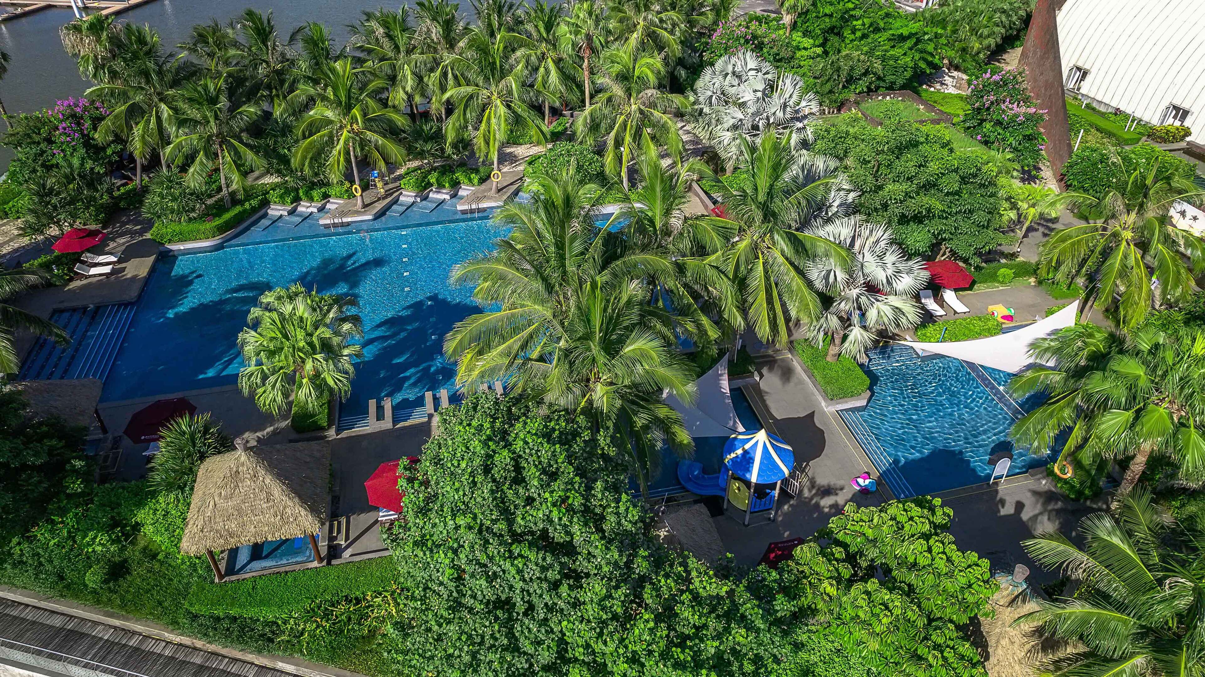 An aerial view of a resort with multiple swimming pools surrounded by lush greenery and palm trees.
