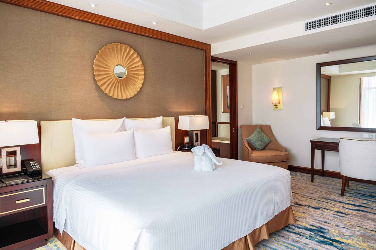 A hotel room with a large bed, a desk, a chair, a mirror, and a wall-mounted decorative piece.