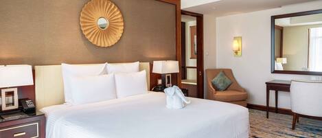 A hotel room with a large bed, a desk, a chair, a mirror, and a wall-mounted decorative piece.