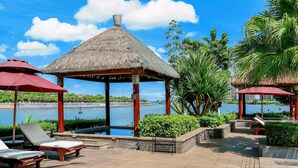 Un espacio exterior tranquilo con un pabellón de techo de paja, sillones de descanso y vista a una masa de agua serena.