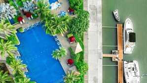 Vista aérea de un resort con una amplia piscina rodeada de palmeras y sillas de descanso.