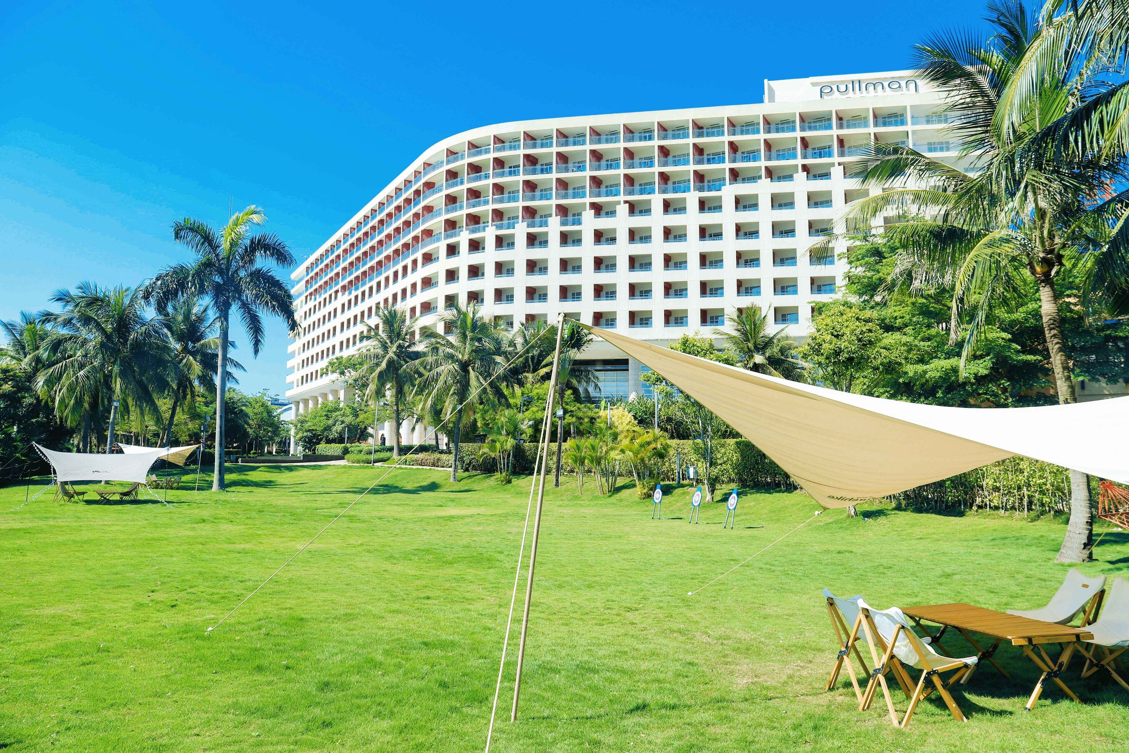 Um hotel com fachada curva, várias varandas e um gramado com área de estar ao ar livre.