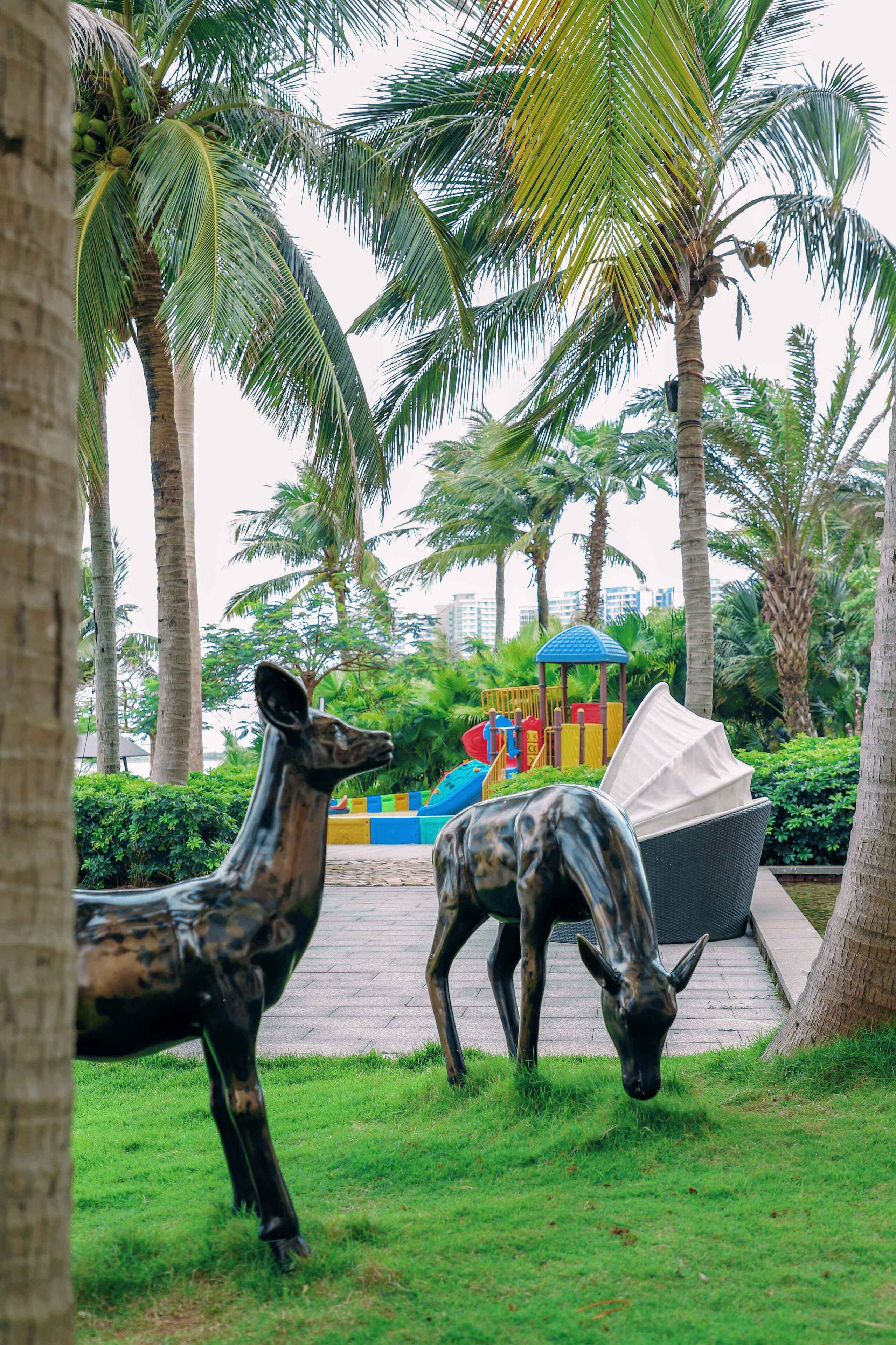 A park with palm trees, a playground, and two statues of deer.