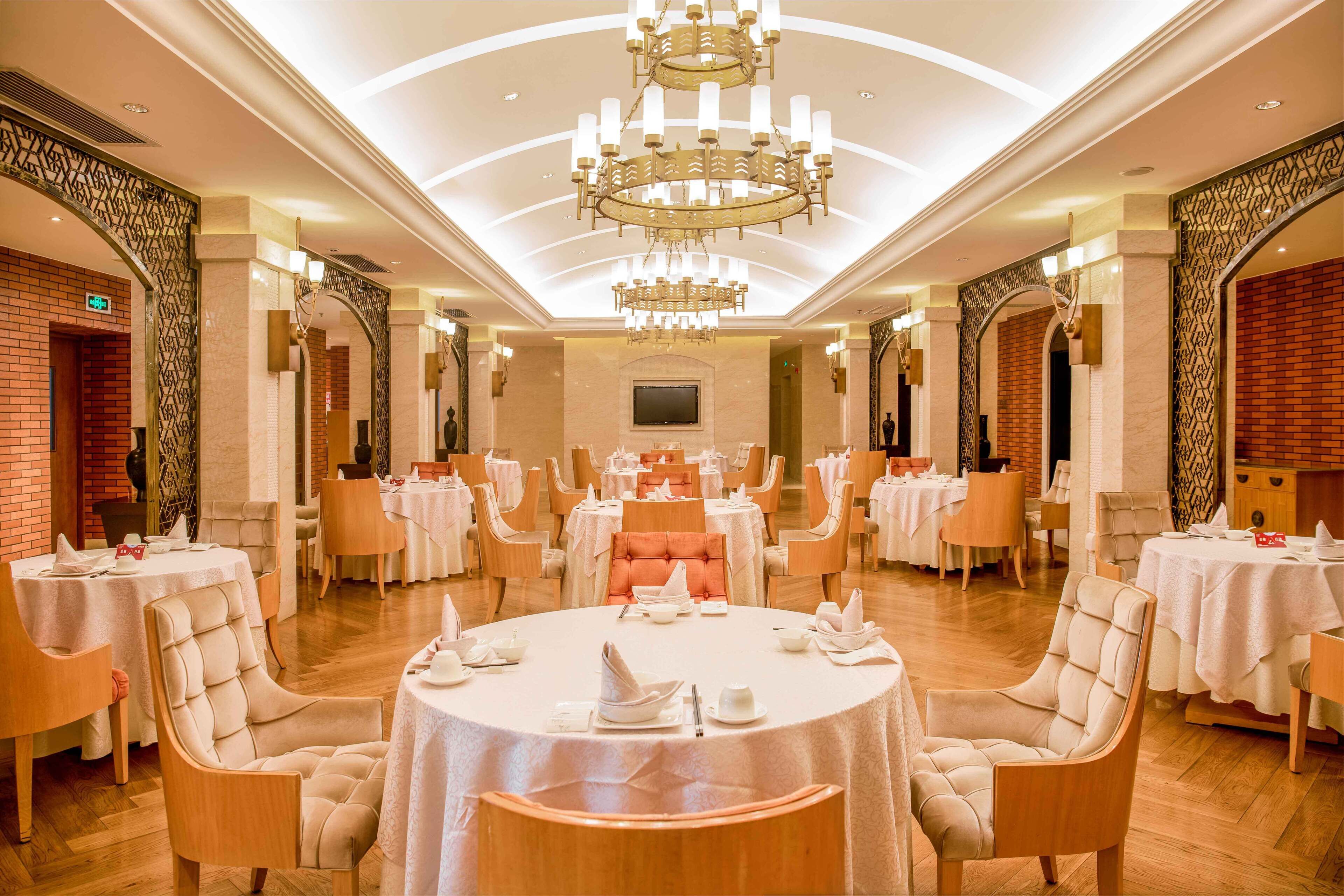 Uma sala de jantar ampla com mesas redondas, cadeiras confortáveis e um grande lustre.
