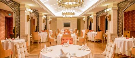 Uma sala de jantar ampla com mesas redondas, cadeiras confortáveis e um grande lustre.