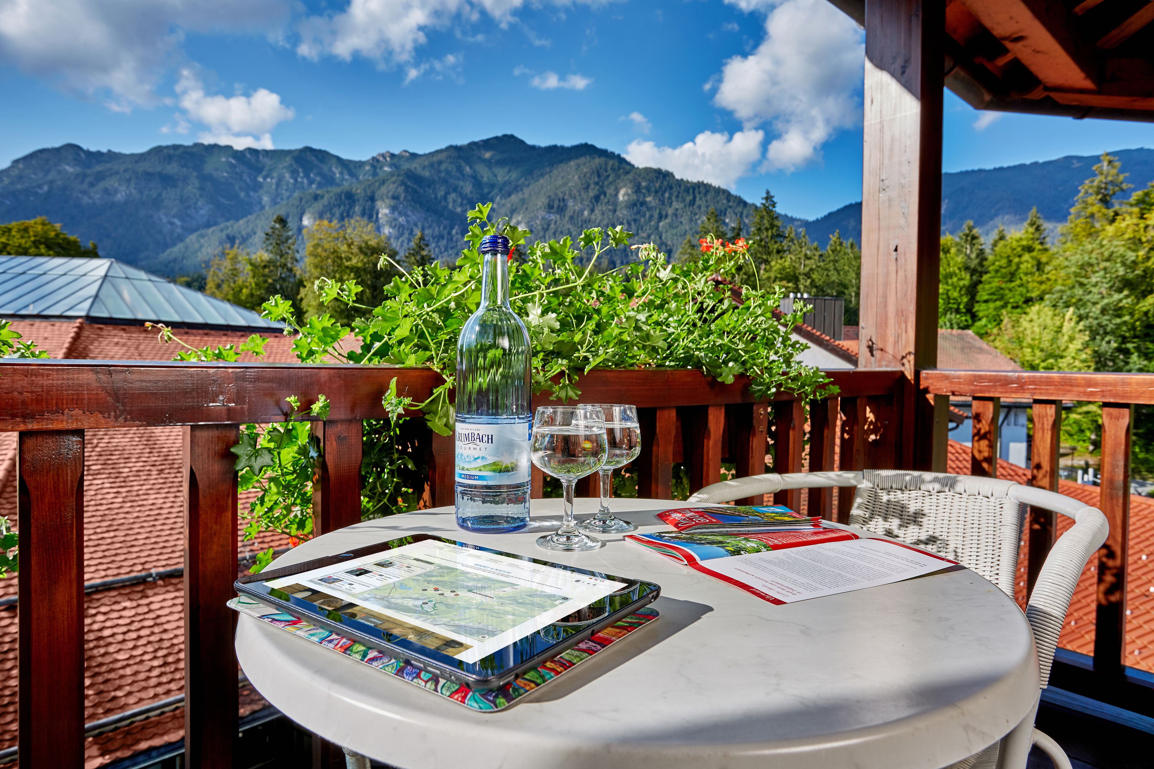 Ein Tisch mit einer Flasche, Gläsern und einer Karte auf einem Balkon mit Blick auf die Berge.