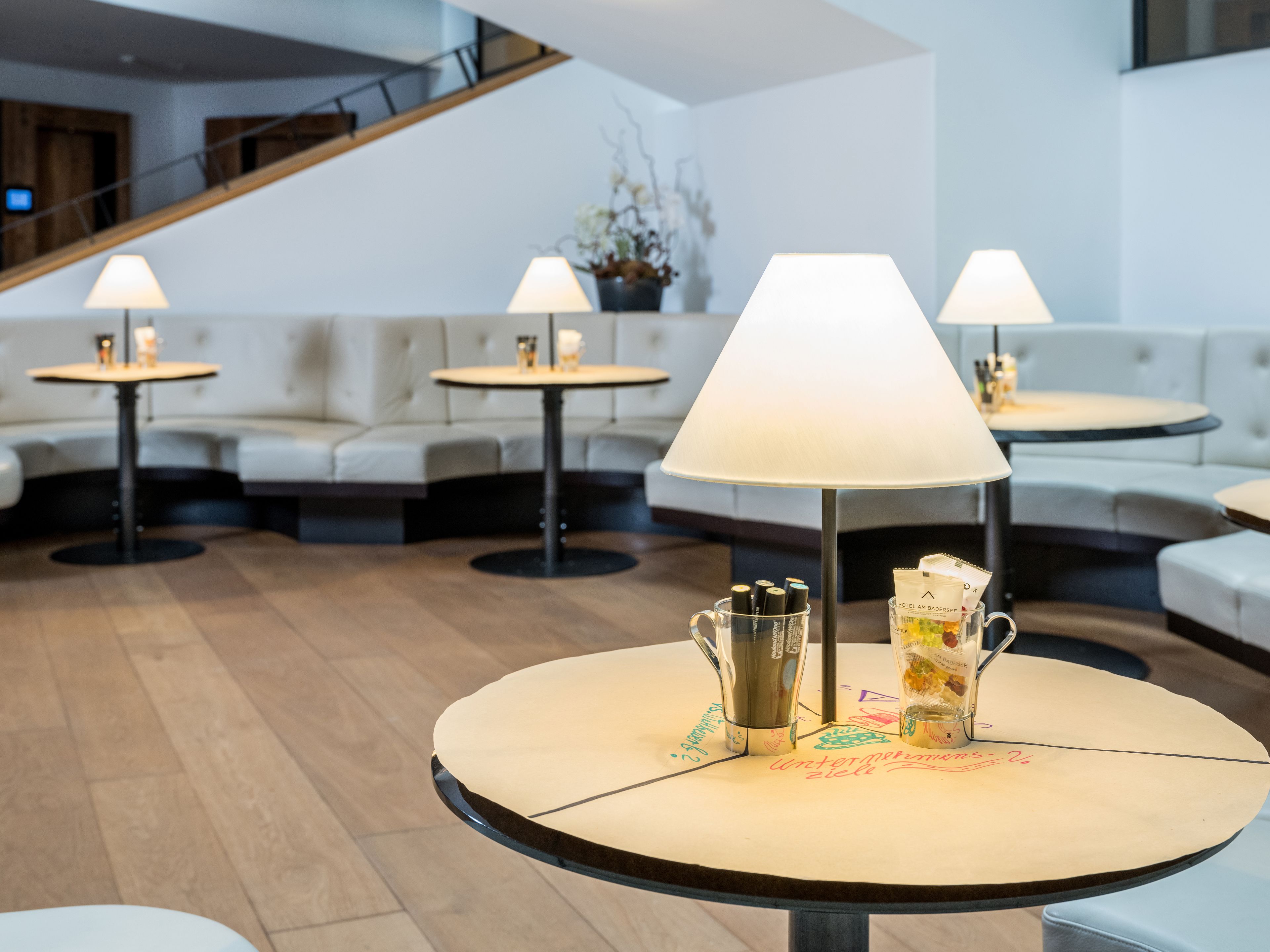 Rebedor modern d'hotel amb taules rodones, cadascuna amb una làmpada i un petit espai per al cafè.