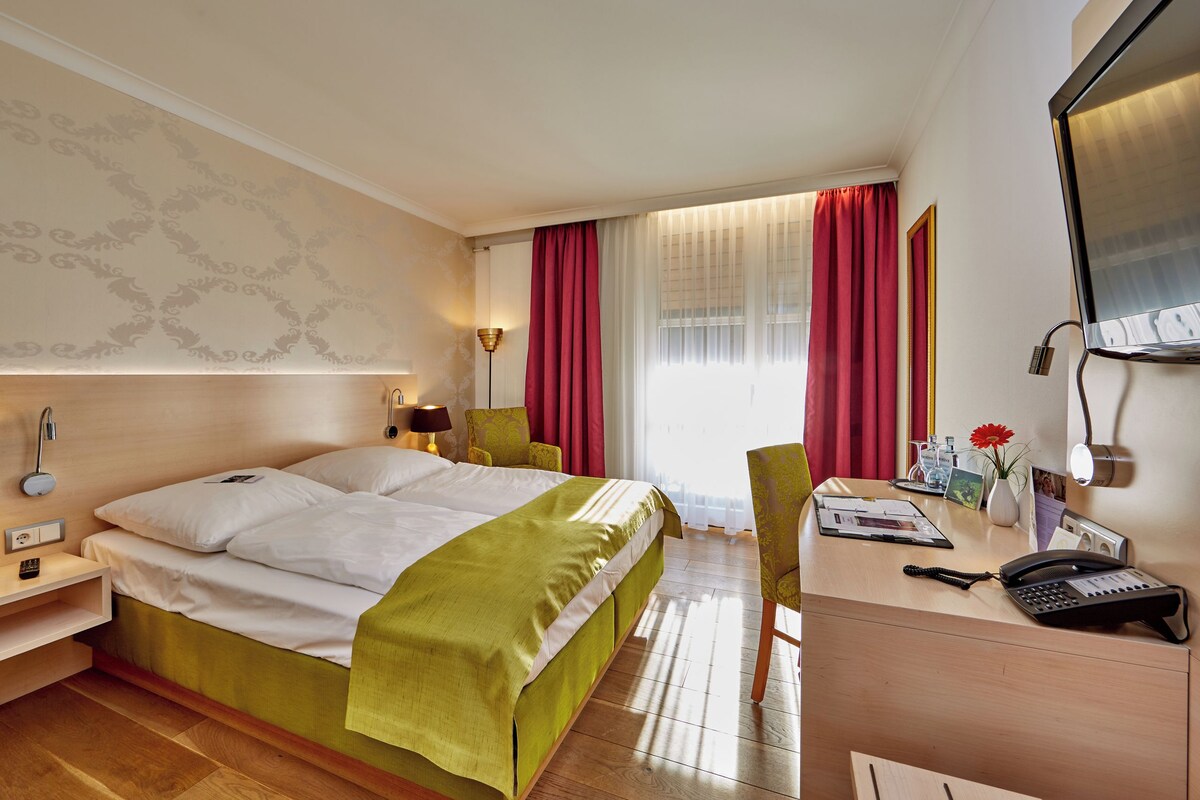 A hotel room with a bed, desk, chair, and a telephone.