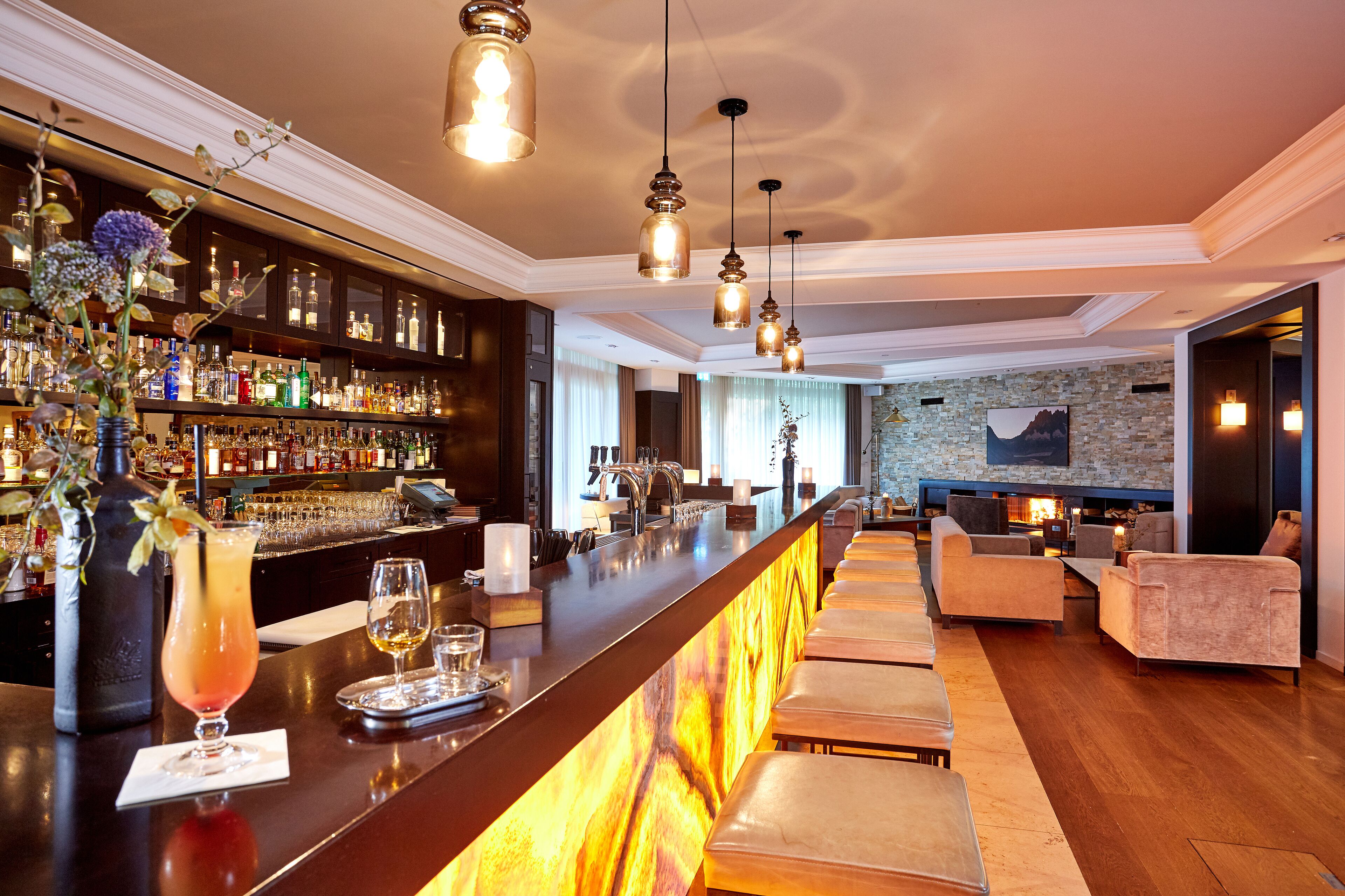A bar area with a long counter, shelves with bottles, and a seating area with sofas and a fireplace.