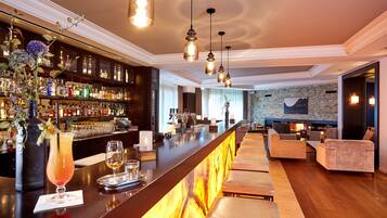 A bar area with a long counter, shelves with bottles, and a seating area with sofas and a fireplace.