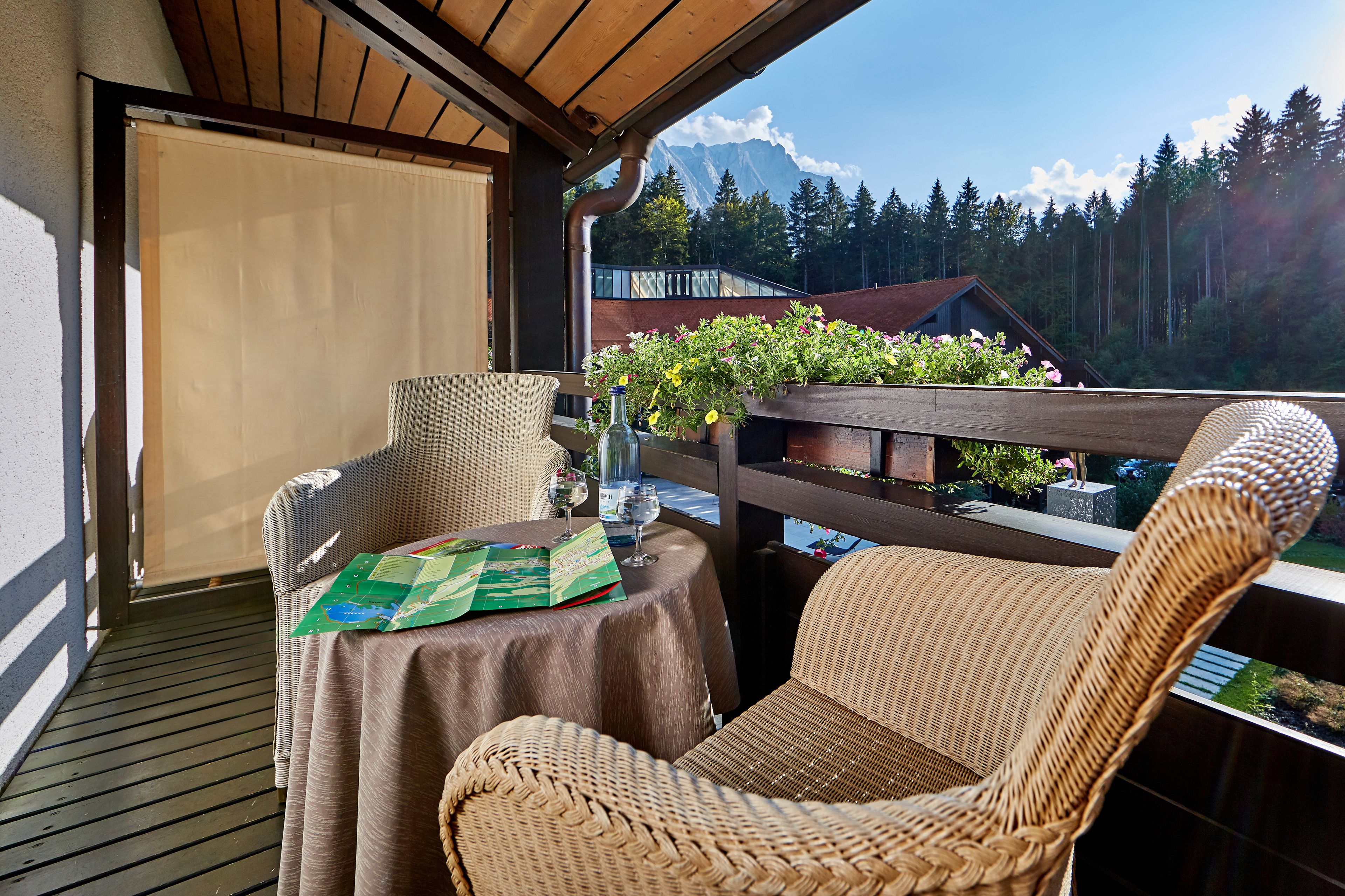 A balcony with wicker chairs, a table with a map, and a view of mountains and trees.