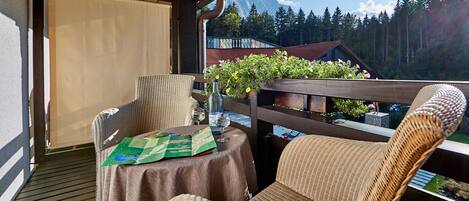 A balcony with wicker chairs, a table with a map, and a view of mountains and trees.