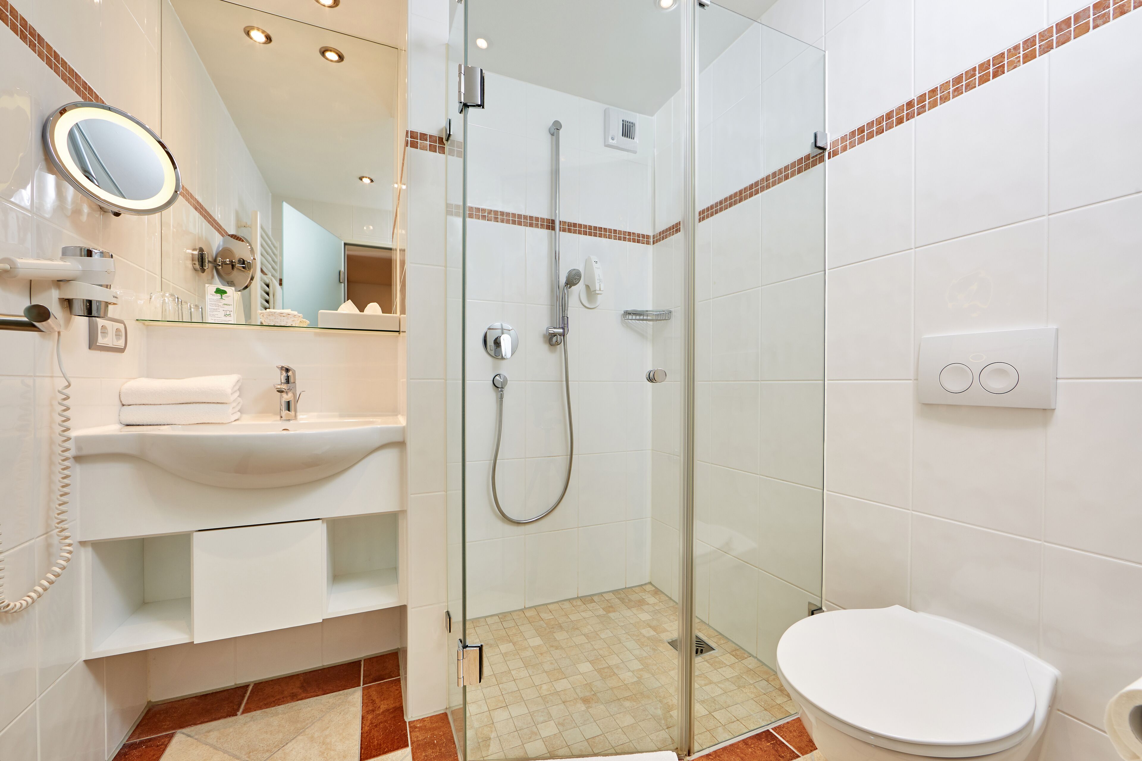 Ein modernes Badezimmer mit einer Glaskabine zur Dusche, einem weißen Waschbecken mit Spiegel und einer Toilette.